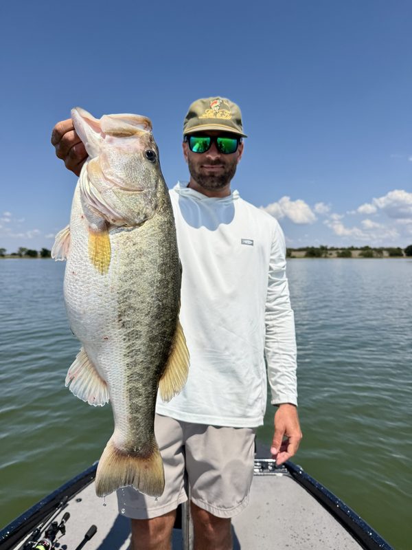Angler standing on the bow of a bass boat holding a big largemouth bass by the jaw