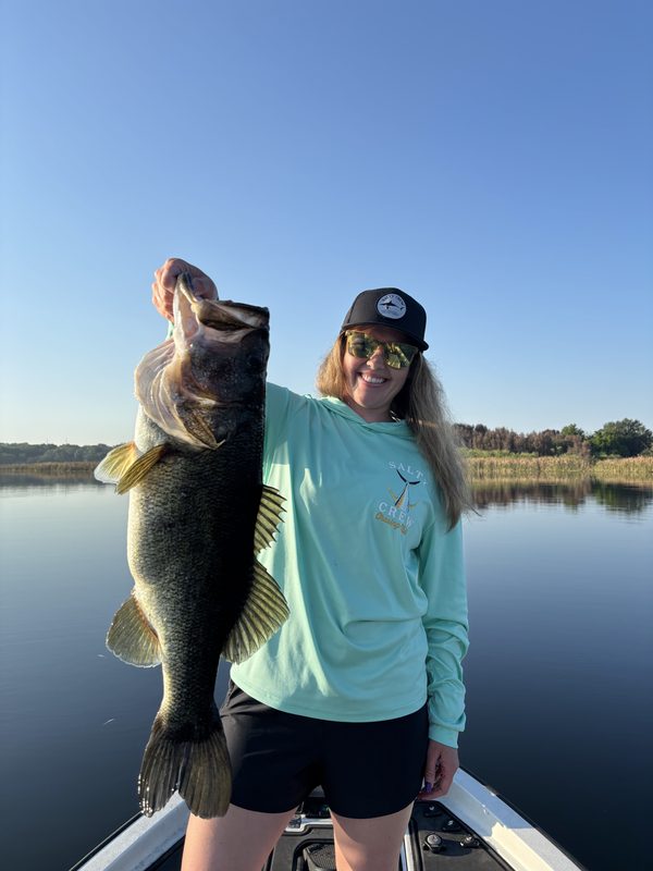 Woman angler holding a big largemouth bass vertically on a calm morning from a bass boat