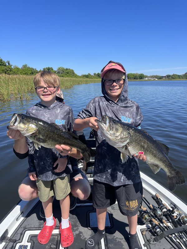 Two young anglers on a bass boat each holding a largemouth bass, Winter Haven Chain of Lakes