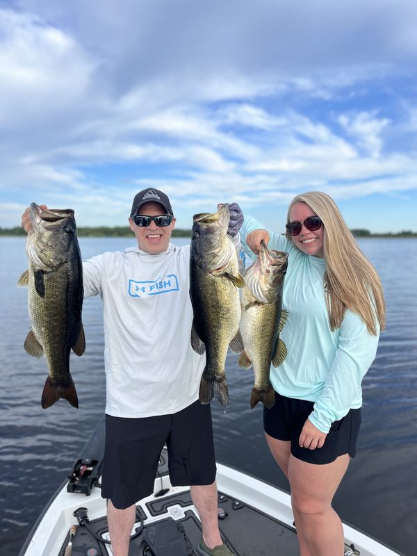 Two anglers on a bass boat holding up three largemouth bass between them