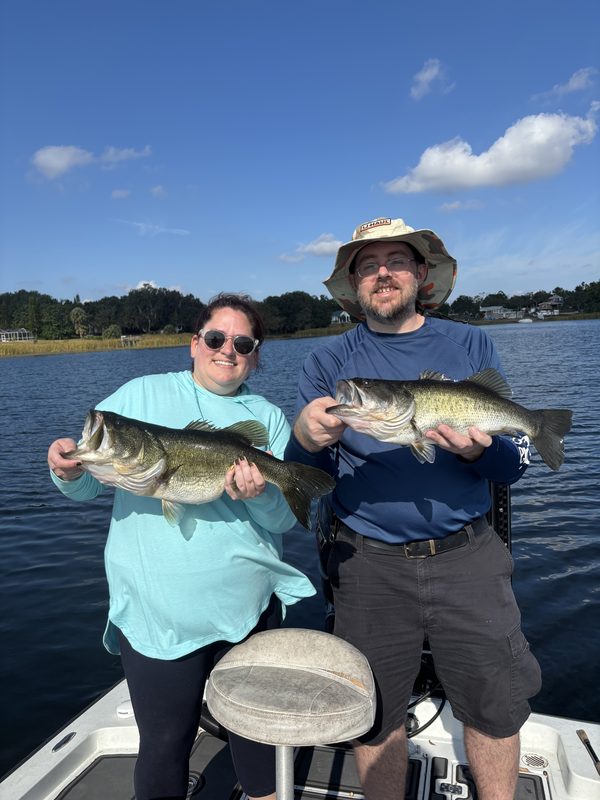 Two anglers on a guided bass charter each holding a largemouth bass on a calm lake