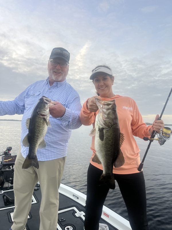 Two anglers on a guided charter each holding a largemouth bass early in the morning