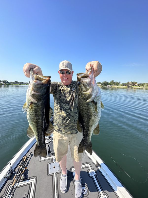 Angler holding two largemouth bass, one in each hand, on the bow of a bass boat, Winter Haven Chain of Lakes