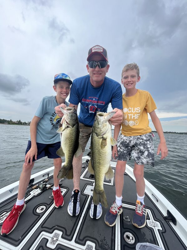 Adult and two young anglers on a bass boat holding two largemouth bass, Winter Haven Chain of Lakes