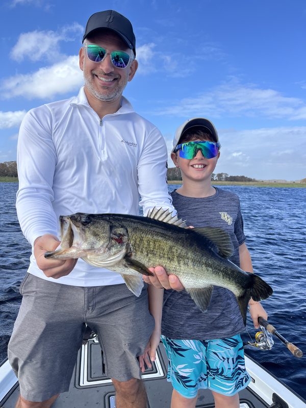 Adult and young angler on a bass boat holding a largemouth bass together