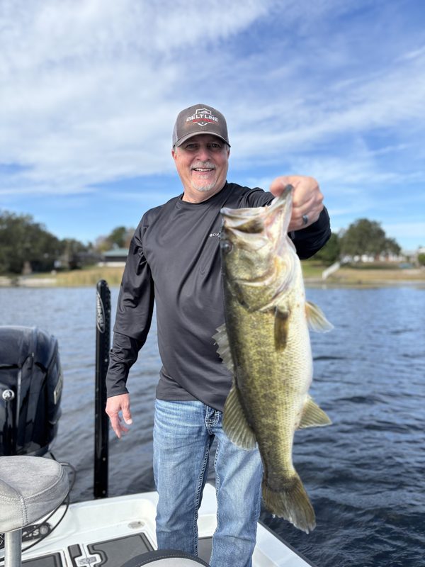 Angler on a guided bass trip holding a largemouth bass on a clear January morning