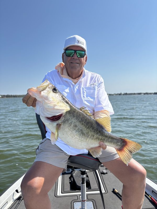 Angler holding a heavy largemouth bass on a spring charter under a clear sky