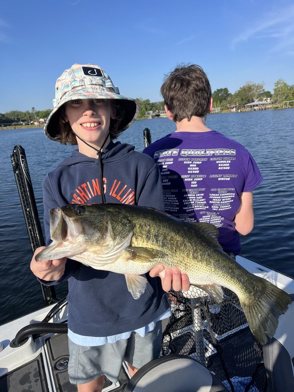 Young angler in a bucket hat holding a big largemouth bass on a guided trip, Winter Haven Chain of Lakes