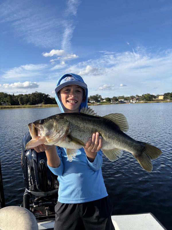 Young angler on a family fishing charter holding a heavy largemouth bass beside the outboard