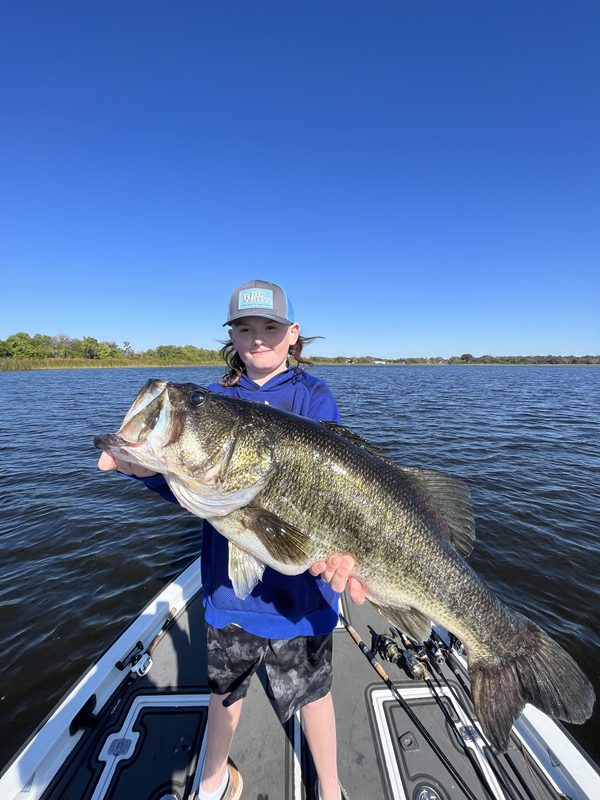 Young angler holding a large largemouth bass with both hands under a deep blue sky, Winter Haven Chain of Lakes