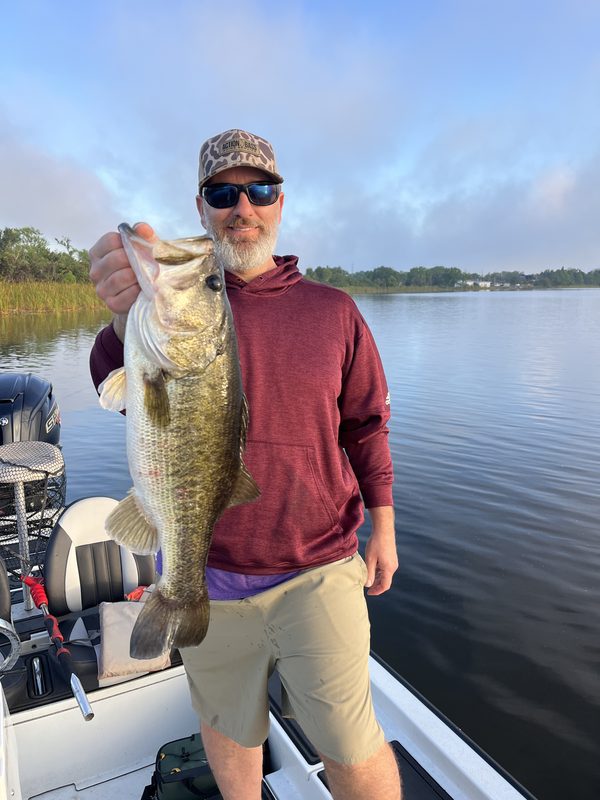 Angler holding a heavy largemouth bass on a calm morning from the deck of a bass boat, Winter Haven Chain of Lakes