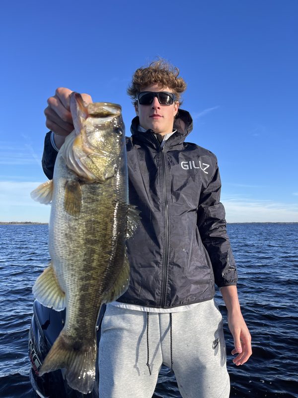 Teenage angler in a jacket holding a largemouth bass on a cold January day