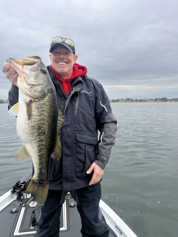 Angler in a rain jacket holding a largemouth bass on an overcast morning, Winter Haven Chain of Lakes