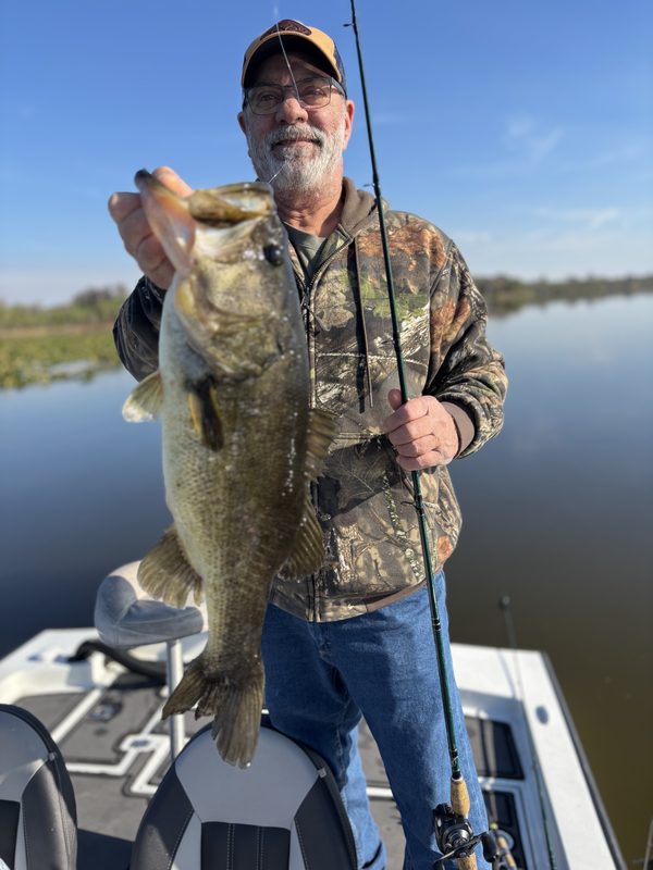 Angler in camo holding a largemouth bass and a spinning rod on a February morning