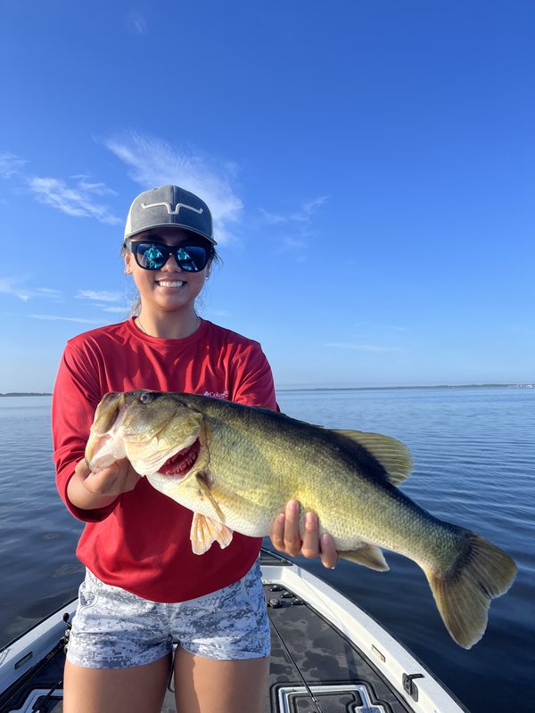 Woman angler holding a long largemouth bass on a bass boat during a summer morning trip