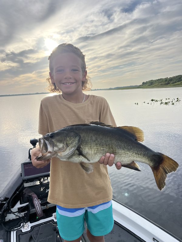 Young angler holding a largemouth bass at golden hour on a calm summer lake