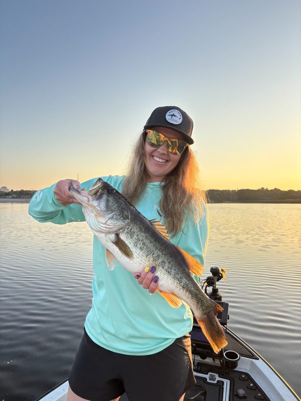 Woman angler holding a largemouth bass at sunrise on a glass-calm lake