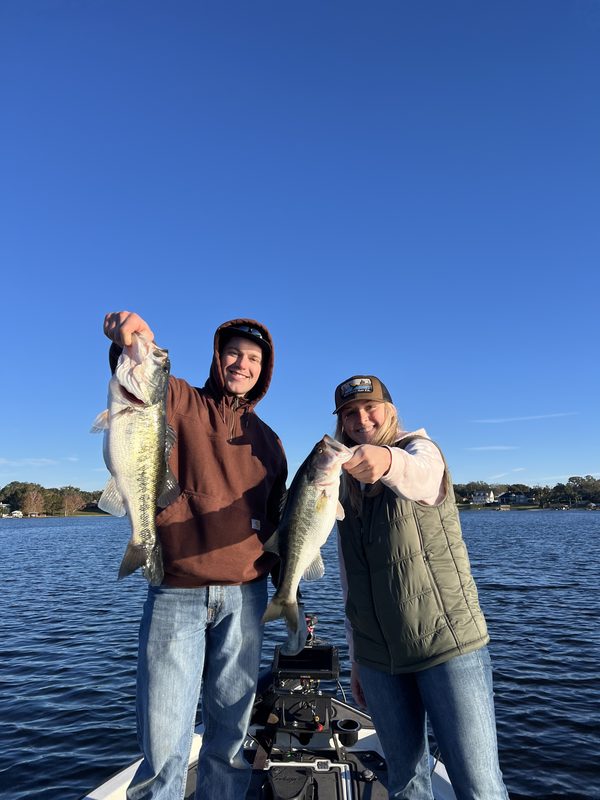 Two anglers on a bass boat holding up two largemouth bass on a bright winter day, Winter Haven Chain of Lakes