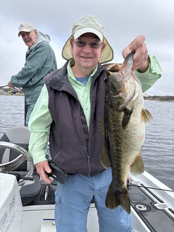 Angler holding a largemouth bass while a second angler fishes behind him on a guided trip