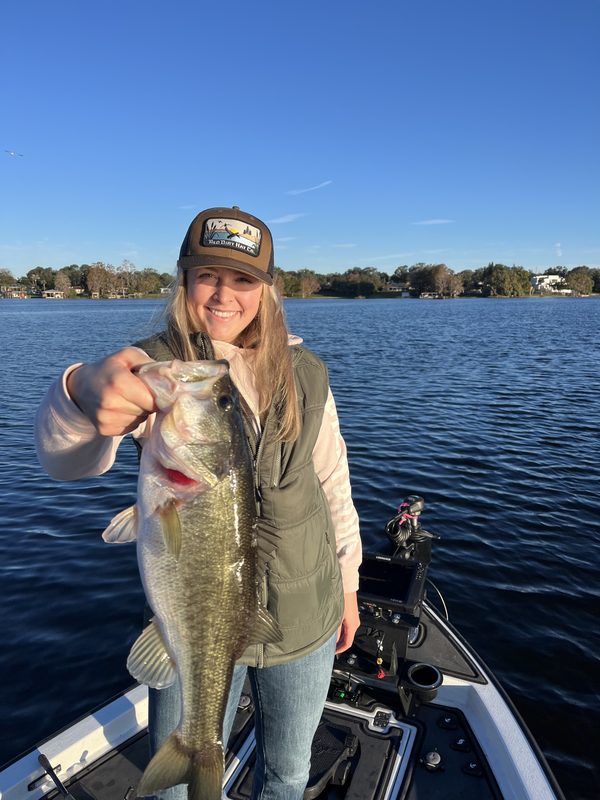 Woman angler in a vest holding a largemouth bass on a cold, clear winter morning, Winter Haven Chain of Lakes