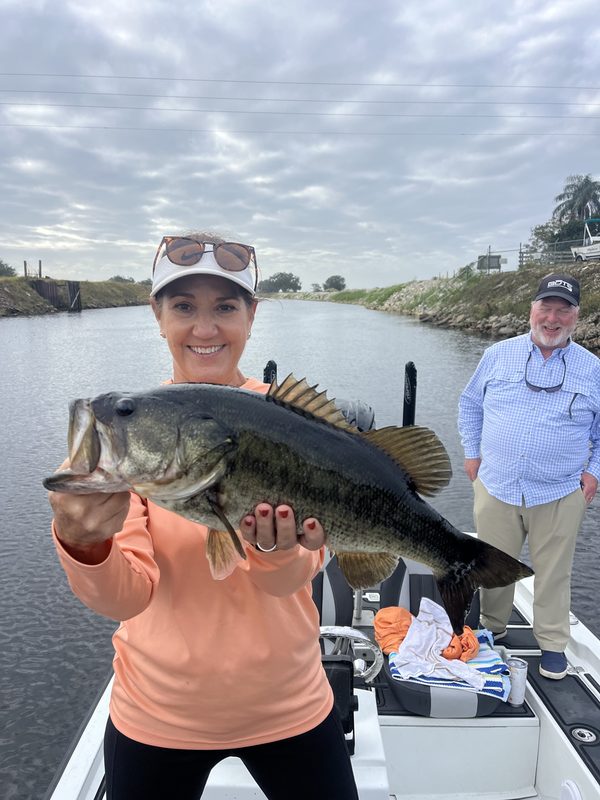 Woman angler holding a wide largemouth bass on a canal trip with a second angler behind