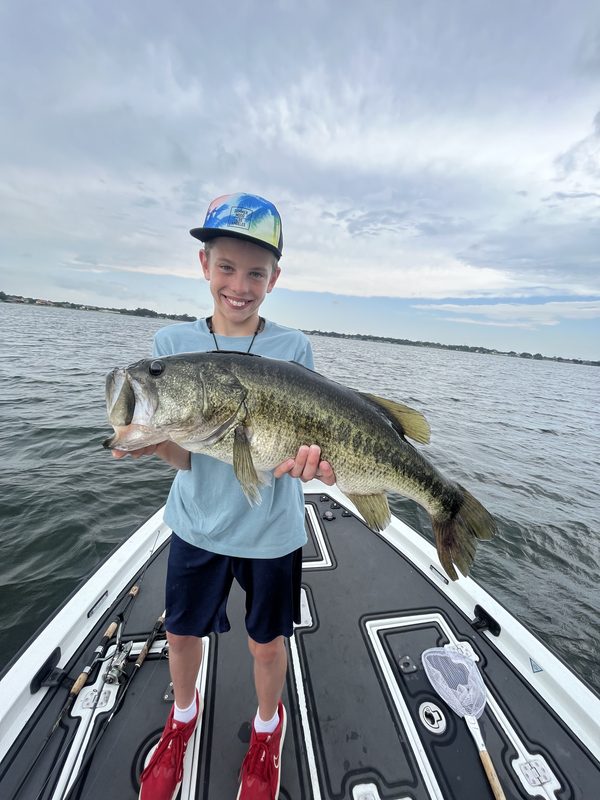 Young angler holding a large largemouth bass with both hands on a bass boat deck, Winter Haven Chain of Lakes